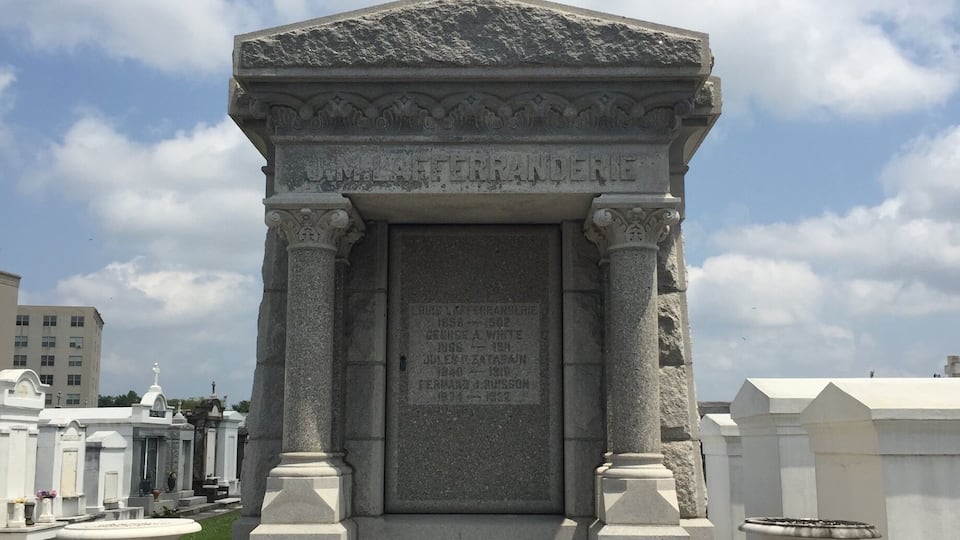 A stone monument with an angel statue on top, featuring inscriptions and a cross base.
