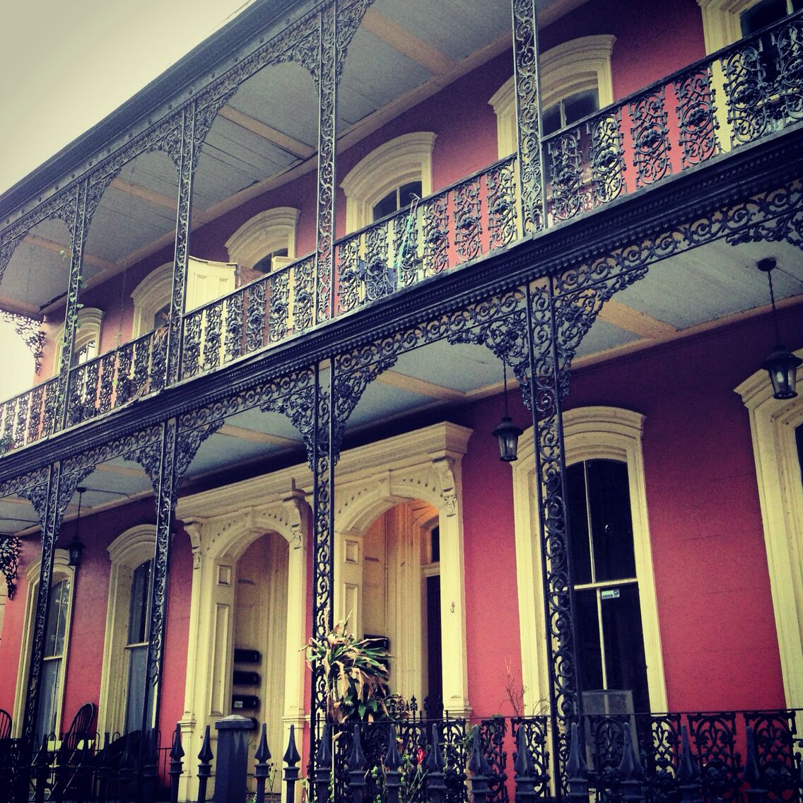 Un edificio rojo con balcones de hierro ornamentados y columnas blancas.
