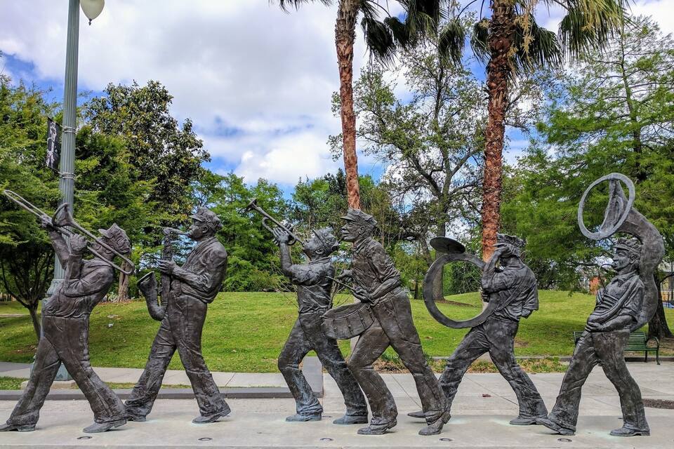 A bronze band sculpture in a park with palm trees and a clear sky.