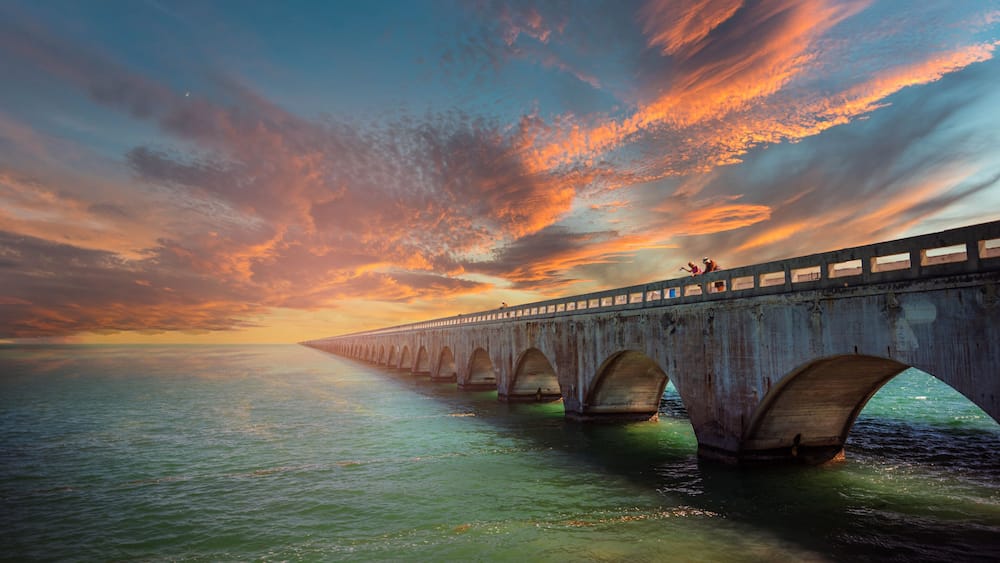 A long bridge with multiple arches over a body of water during sunset.