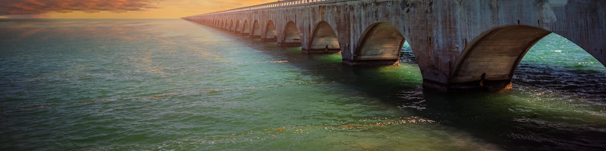 Un long pont, doté de nombreuses arches, enjambant une étendue d’eau au coucher du soleil.