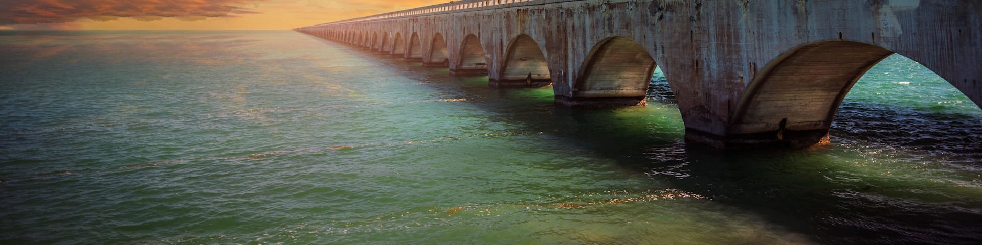 A long bridge with multiple arches over a body of water during sunset.