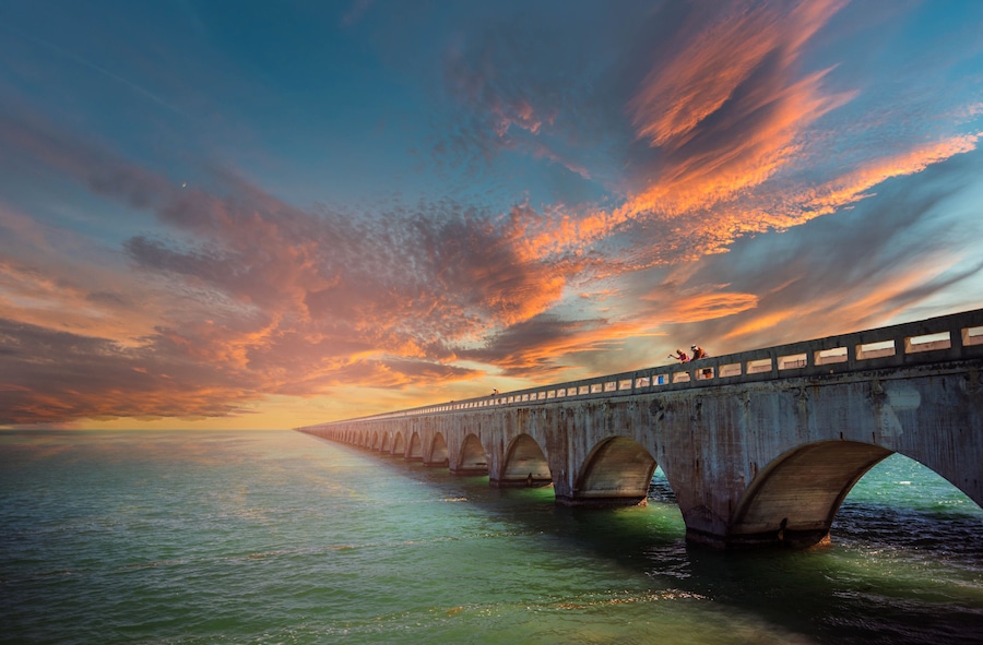A long bridge with multiple arches over a body of water during sunset.
