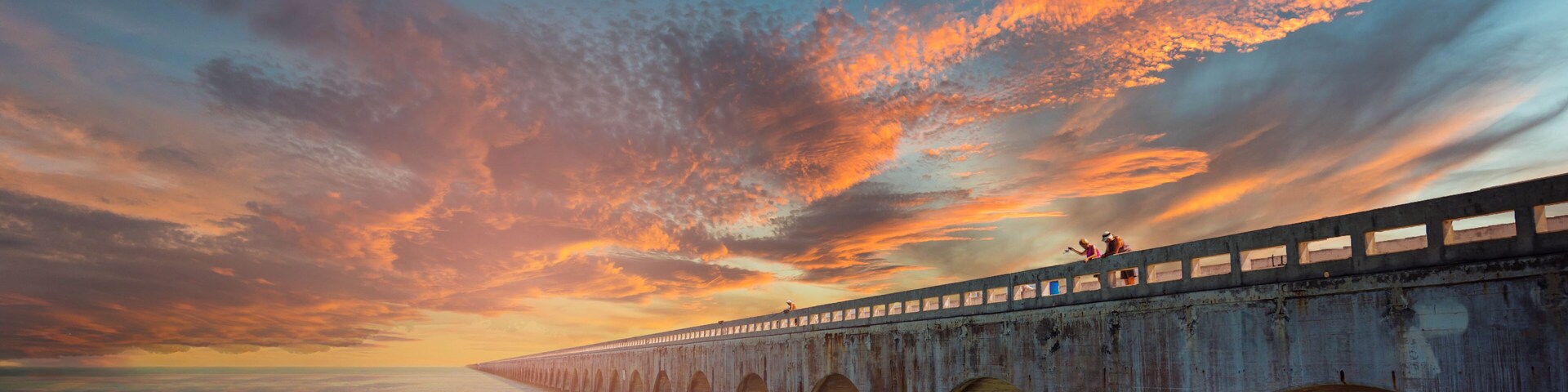 Un puente extenso con múltiples arcos sobre un cuerpo de agua al atardecer.