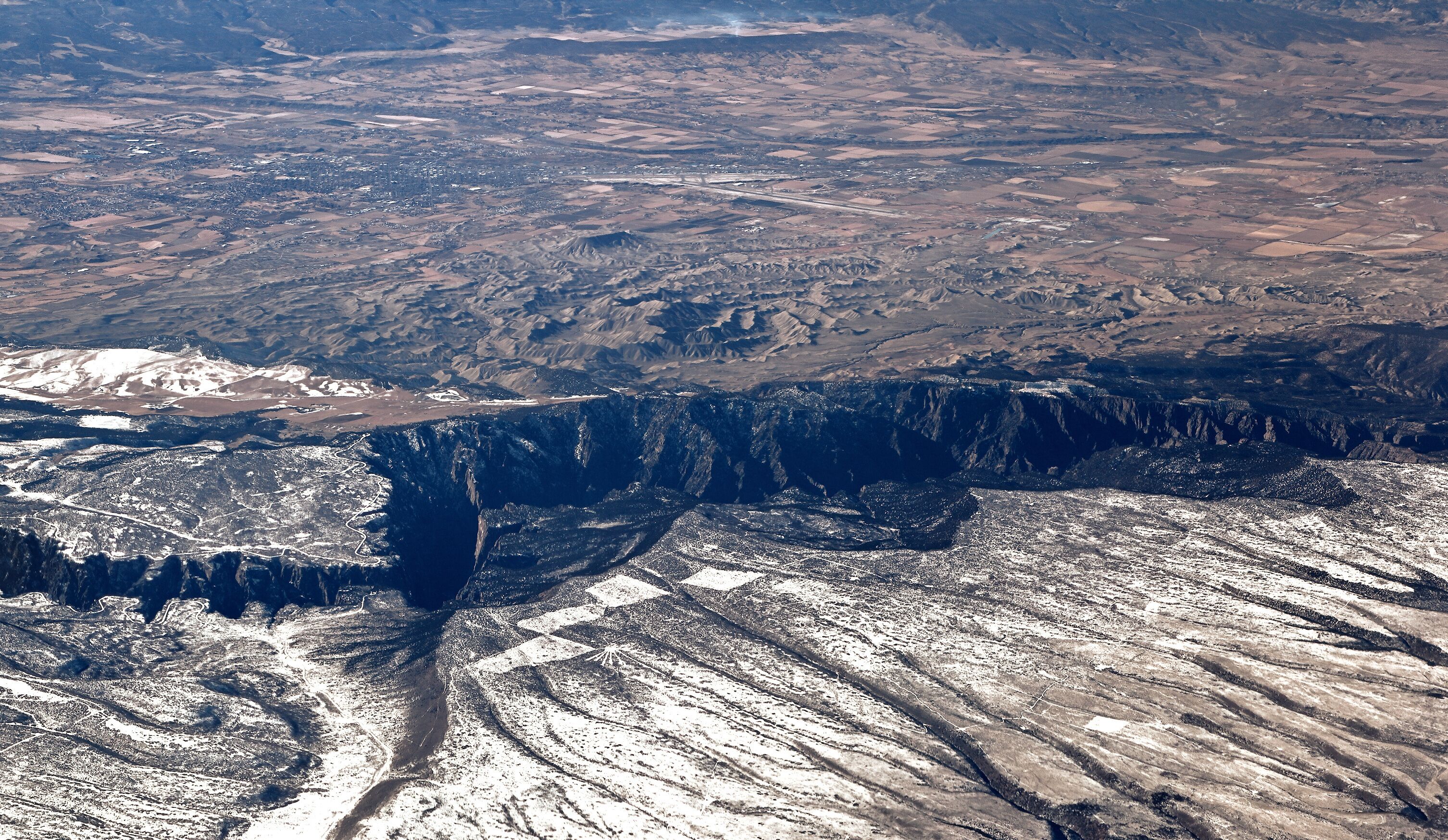 A vast canyon with rugged terrain and a winding road.