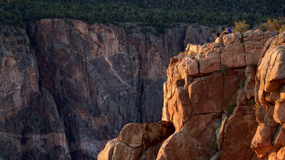 A rugged cliff with large boulders and a forested hill in the background.