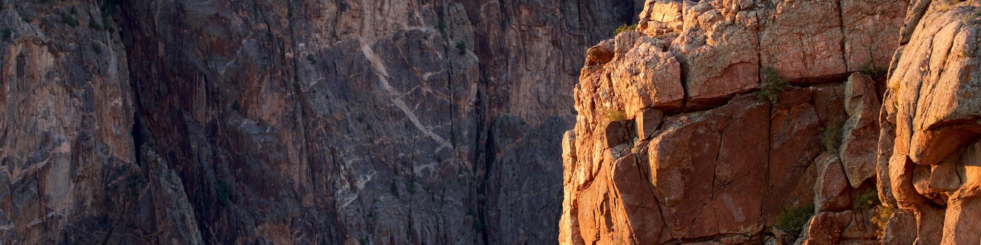 A rugged cliff with large boulders and a forested hill in the background.