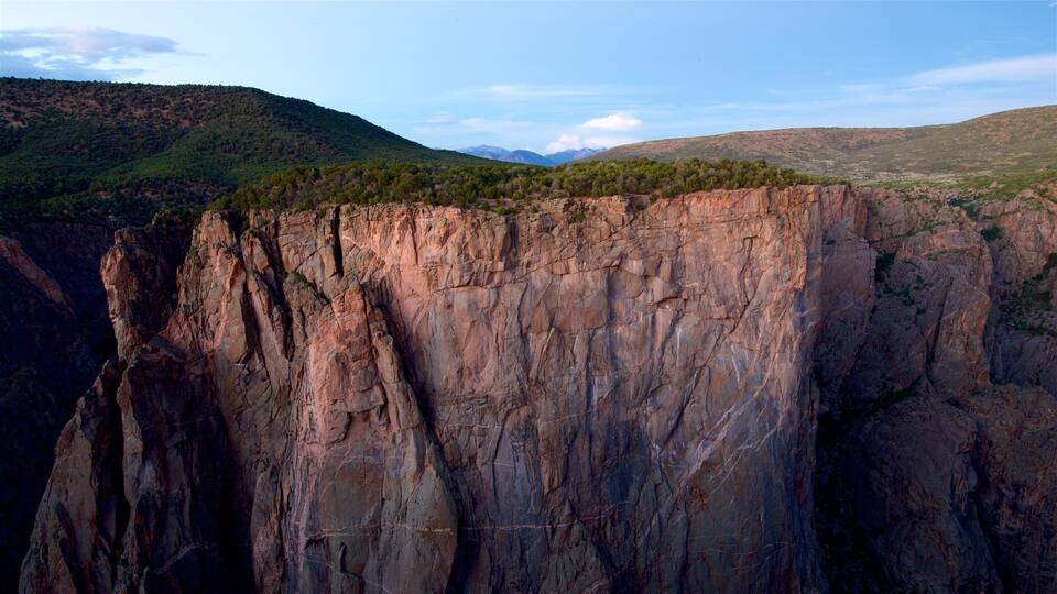 A rugged cliff with a forested hill in the background.