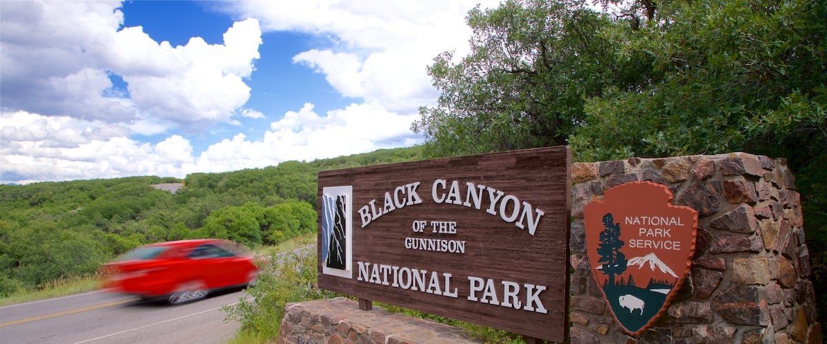 A sign for Black Canyon of the Gunnison National Park with a red car passing by.