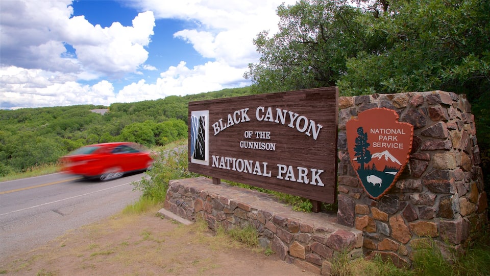 A sign for Black Canyon of the Gunnison National Park with a red car passing by.