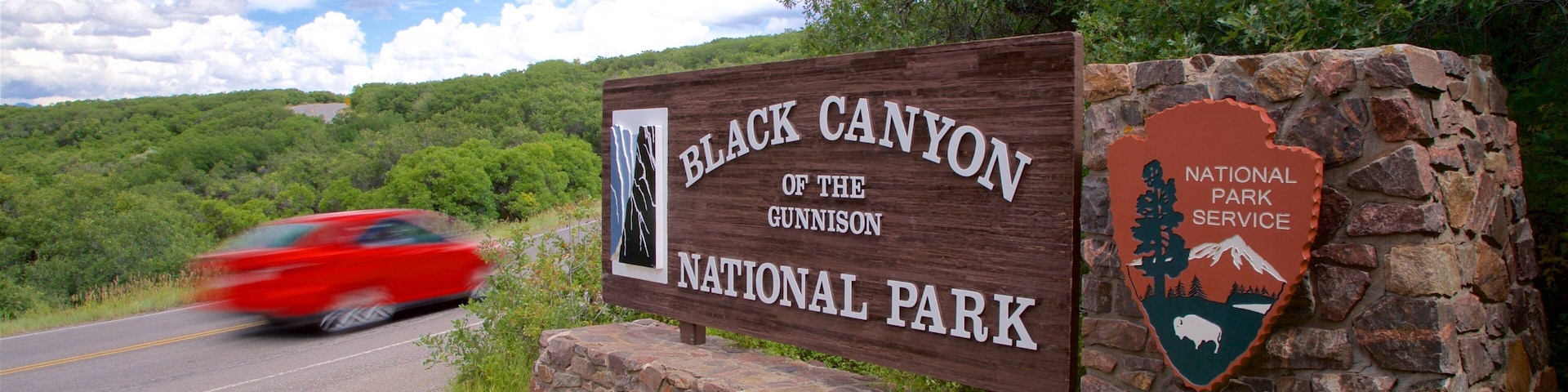 Placa do Parque Nacional Black Canyon do Gunnison, com um carro vermelho passando.