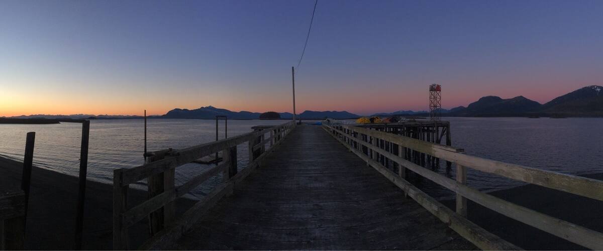 A wooden pier extending into calm waters at sunset with mountains in the background.
