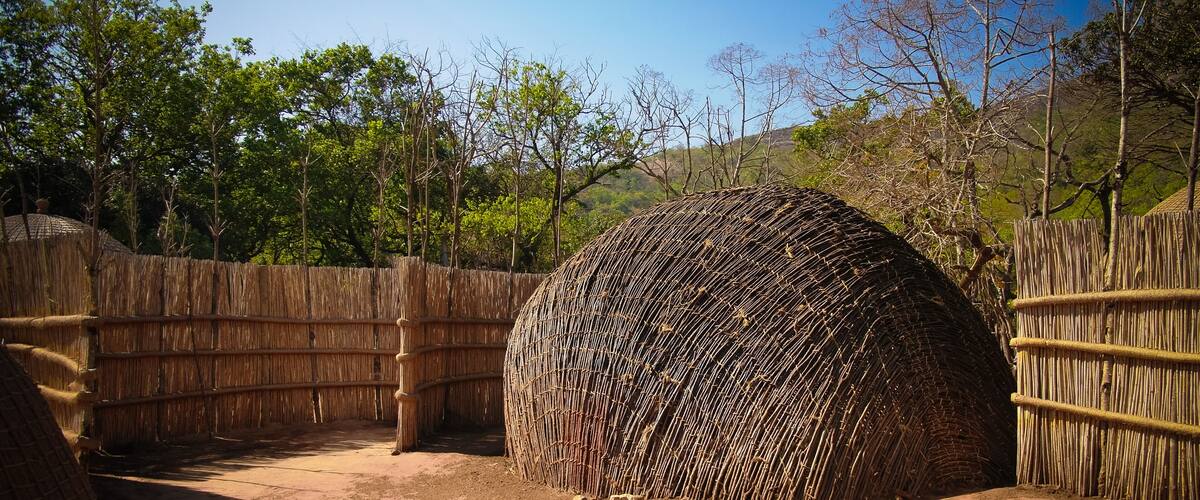 A large, spherical structure made of sticks, surrounded by a bamboo fence in a dry, open area with sparse trees.