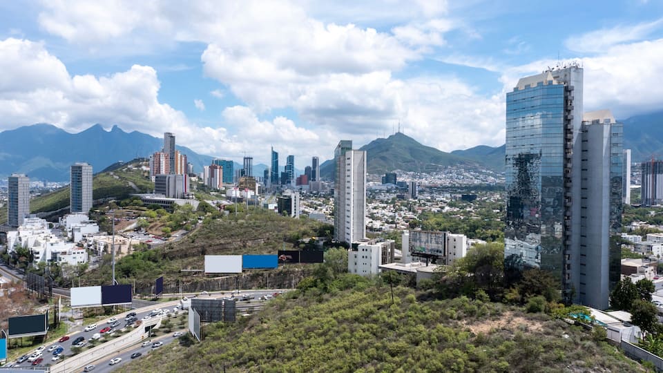 A cityscape with modern buildings, a highway, and mountains in the background.