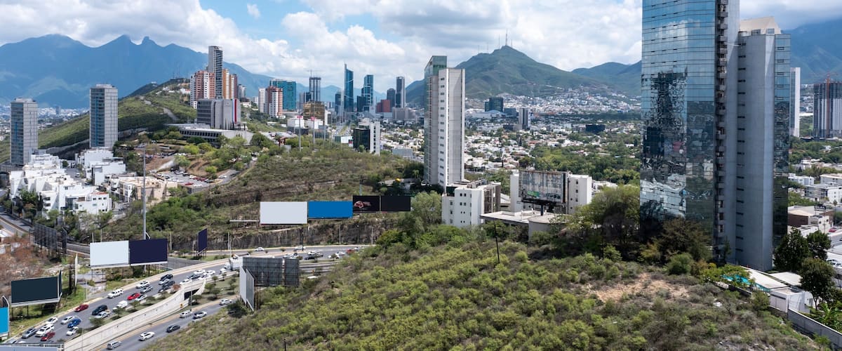 A cityscape with modern buildings, a highway, and mountains in the background.