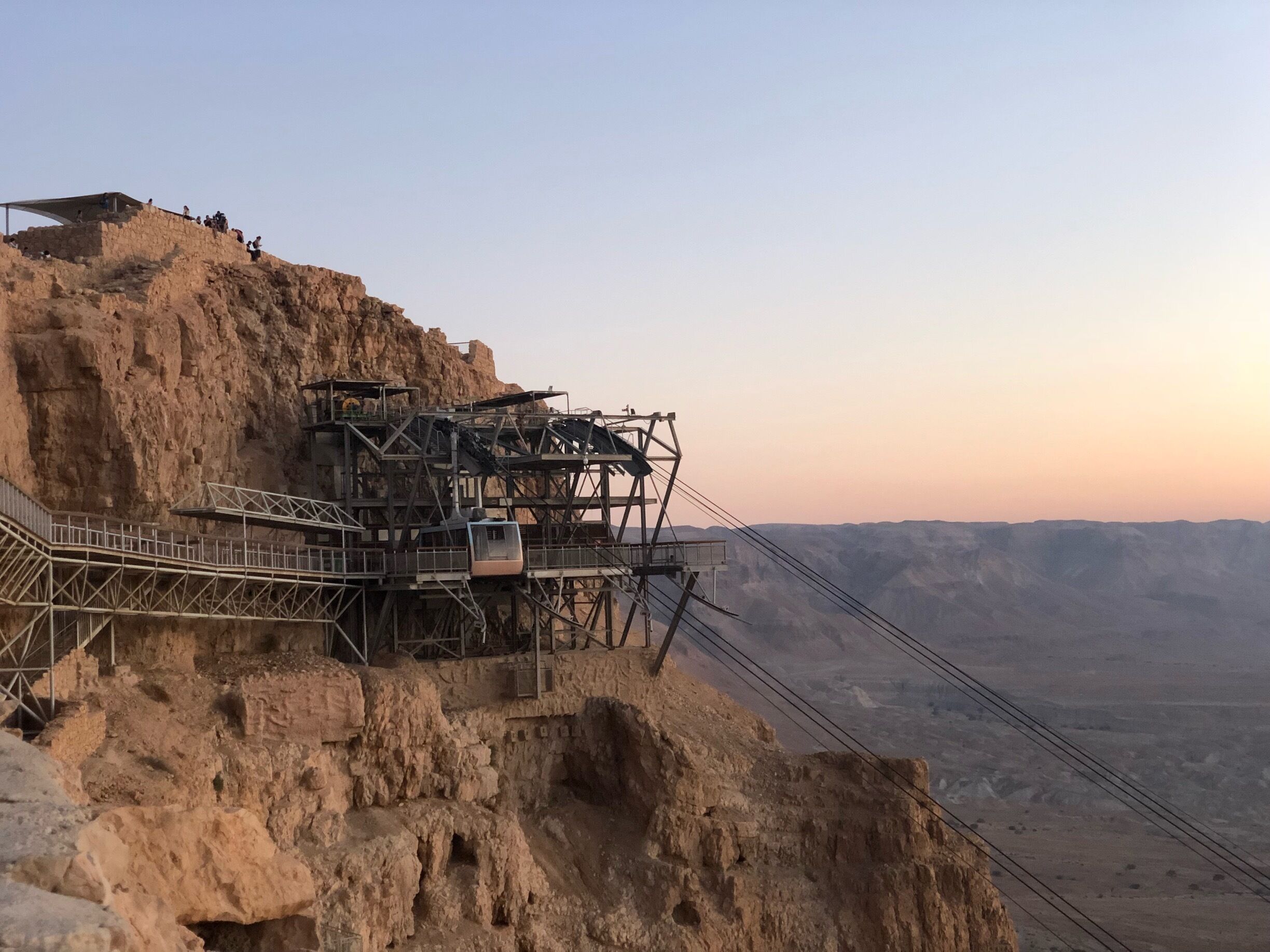 A cable car system on a rocky cliff with a desert landscape in the background.