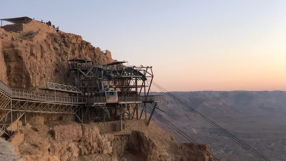 A cable car system on a rocky cliff with a desert landscape in the background.