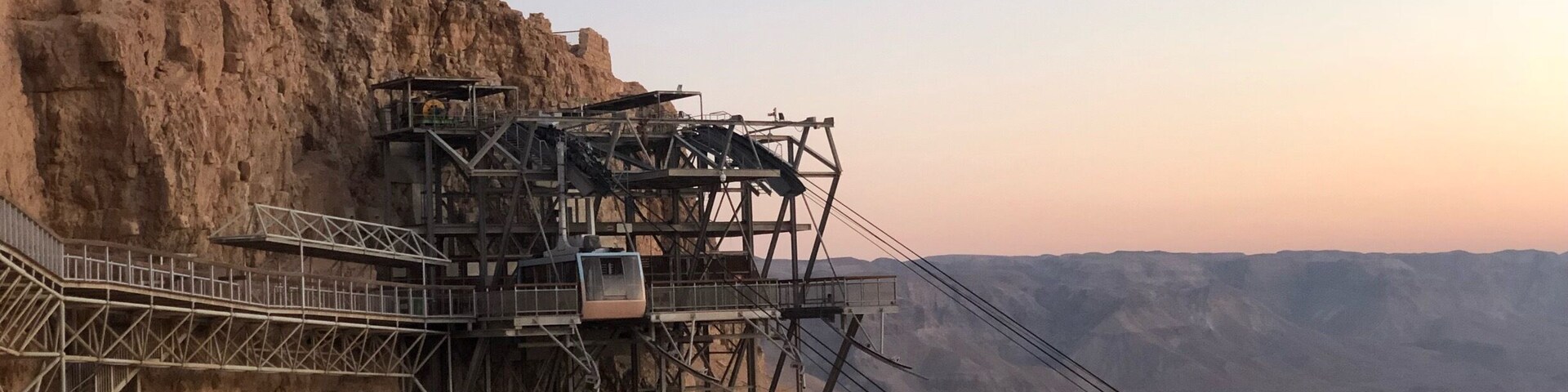 Un sistema de teleférico sobre un risco rocoso, con un paisaje desértico al fondo.