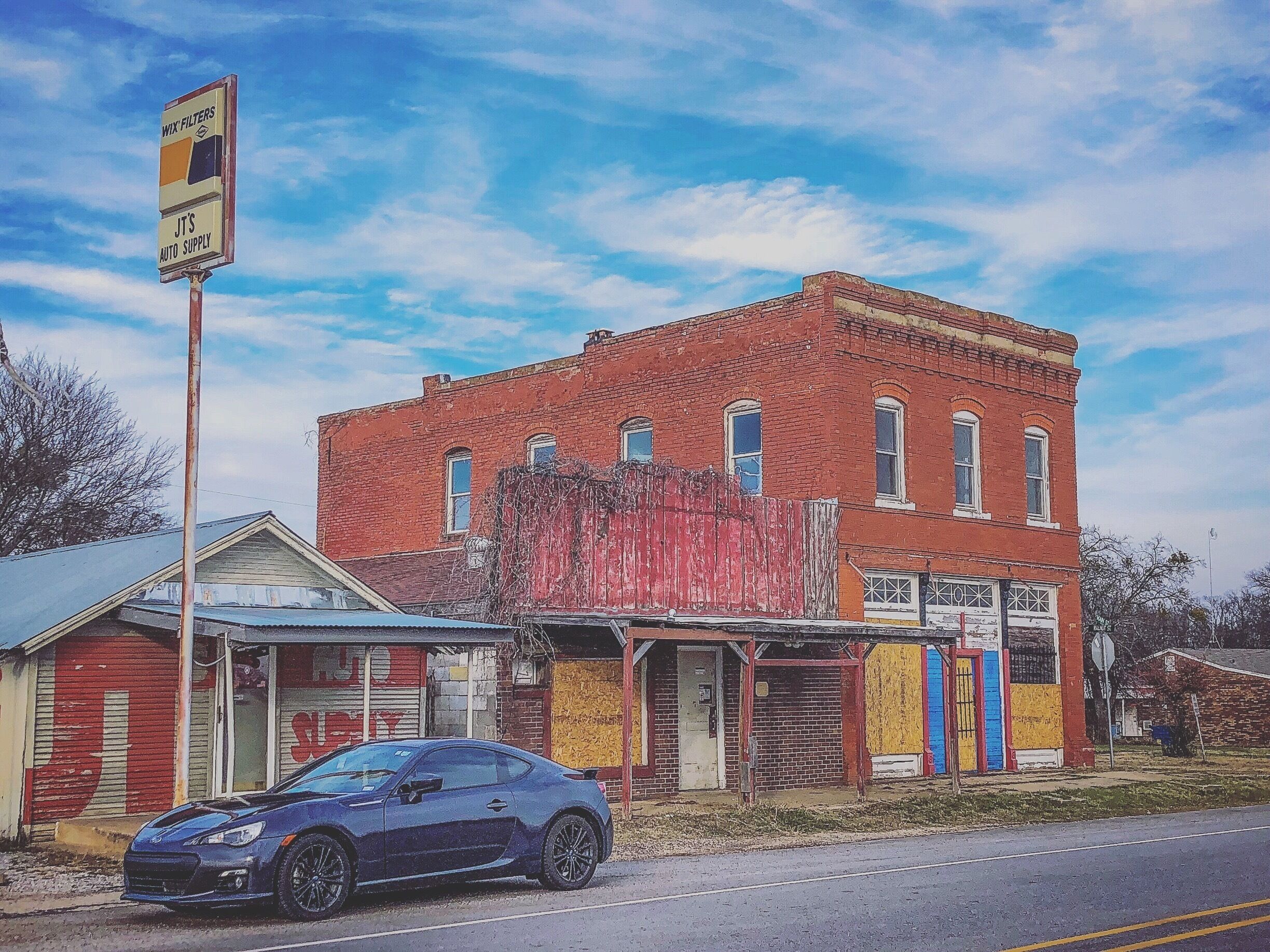 A red brick building with a blue car parked in front.