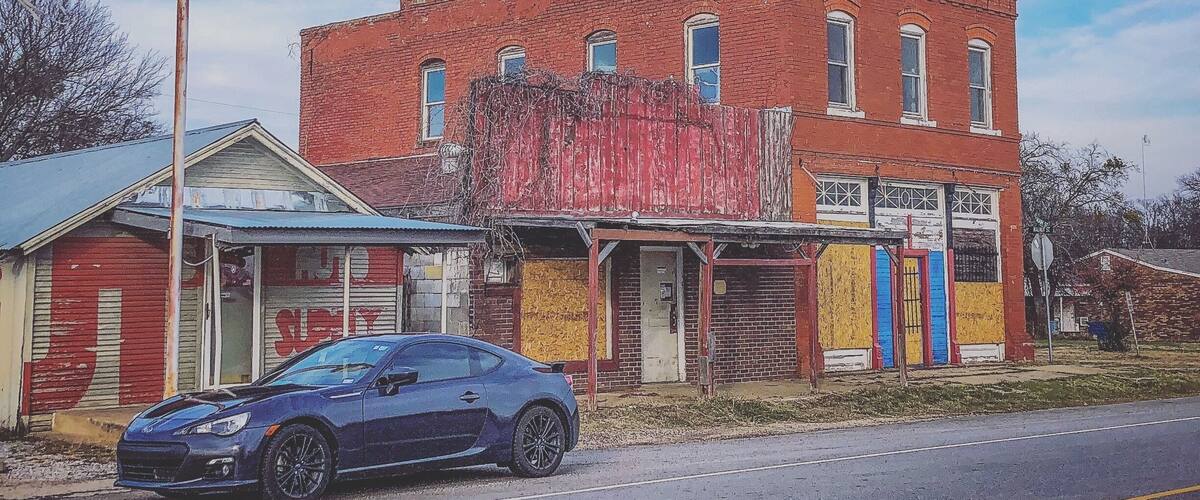 A red brick building with a blue car parked in front.