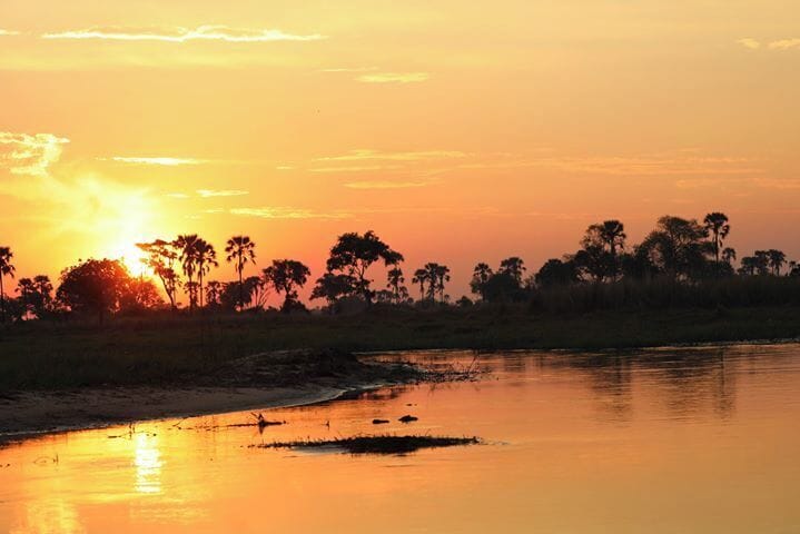 Un atardecer sobre un río, con árboles silueteados contra el cielo.