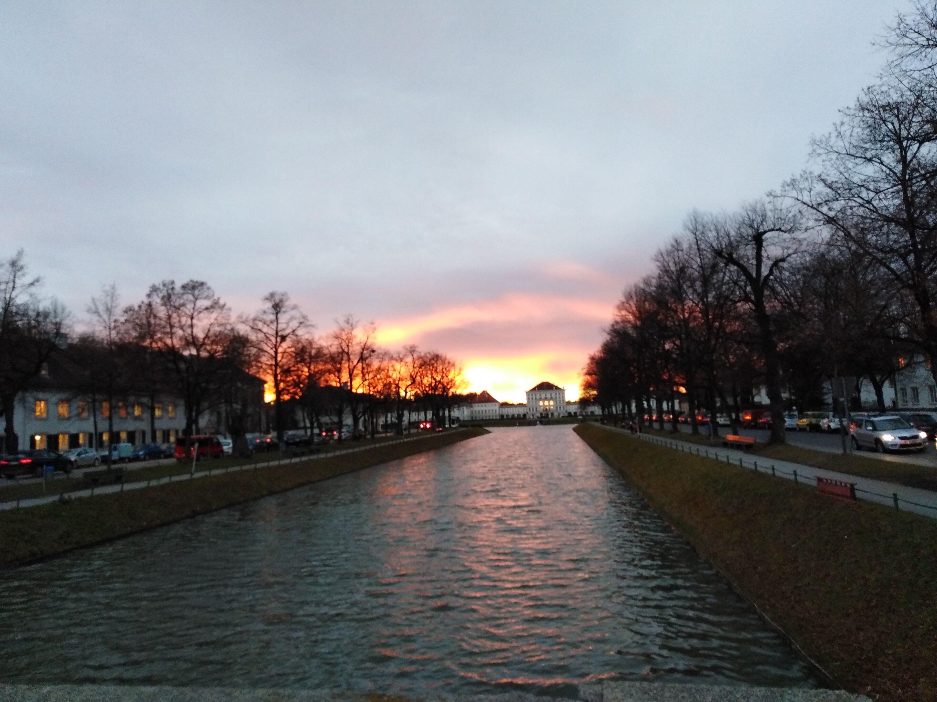 Um canal com o pôr do sol ao fundo, cercado por árvores e edifícios.
