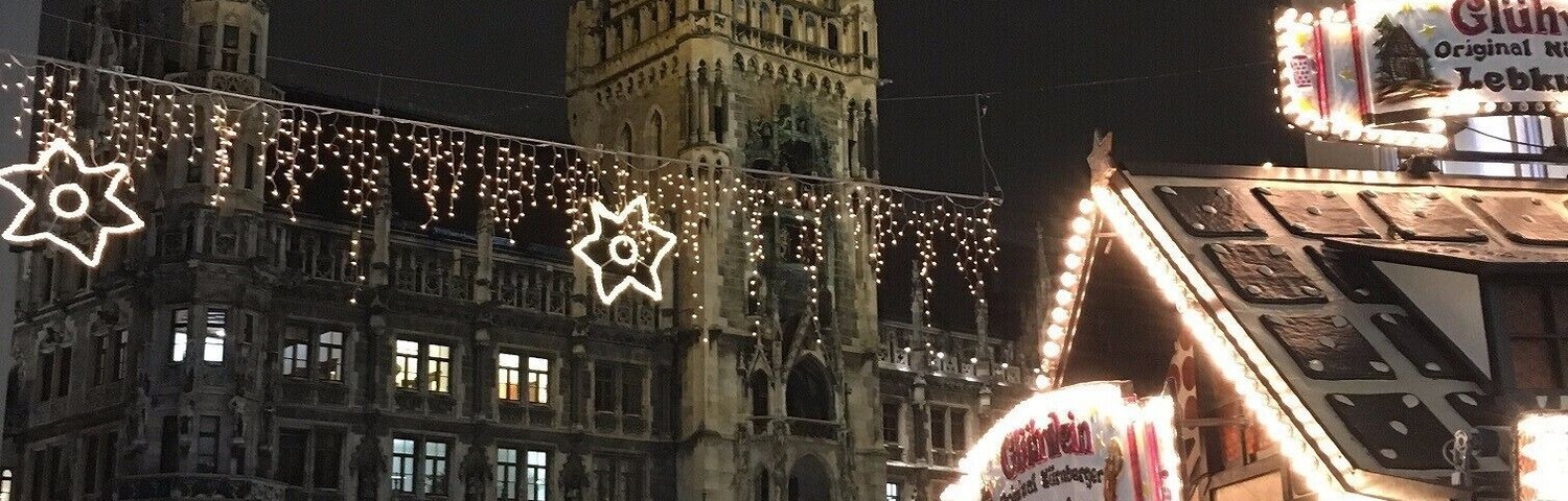 Un edificio histórico con una torre de reloj, rodeado de luces festivas y una multitud de gente.