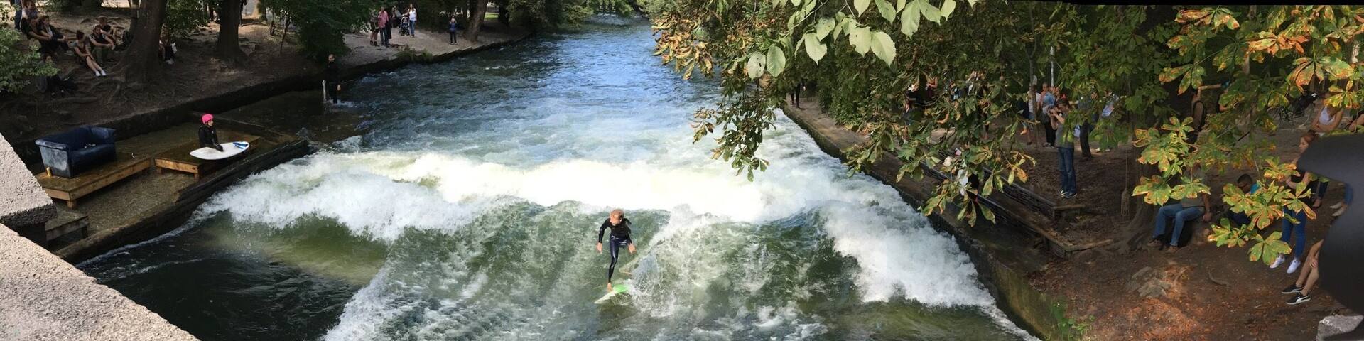 A river with a man surfing, surrounded by trees and a viewing platform.