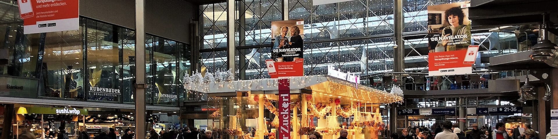 A busy indoor public space with people walking, a kiosk, and various signs.