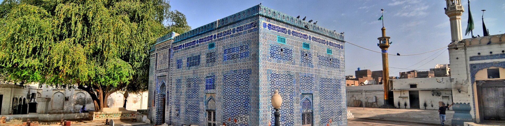 Una mezquita con patrones de azulejos azules, un minarete y un árbol en un patio.
