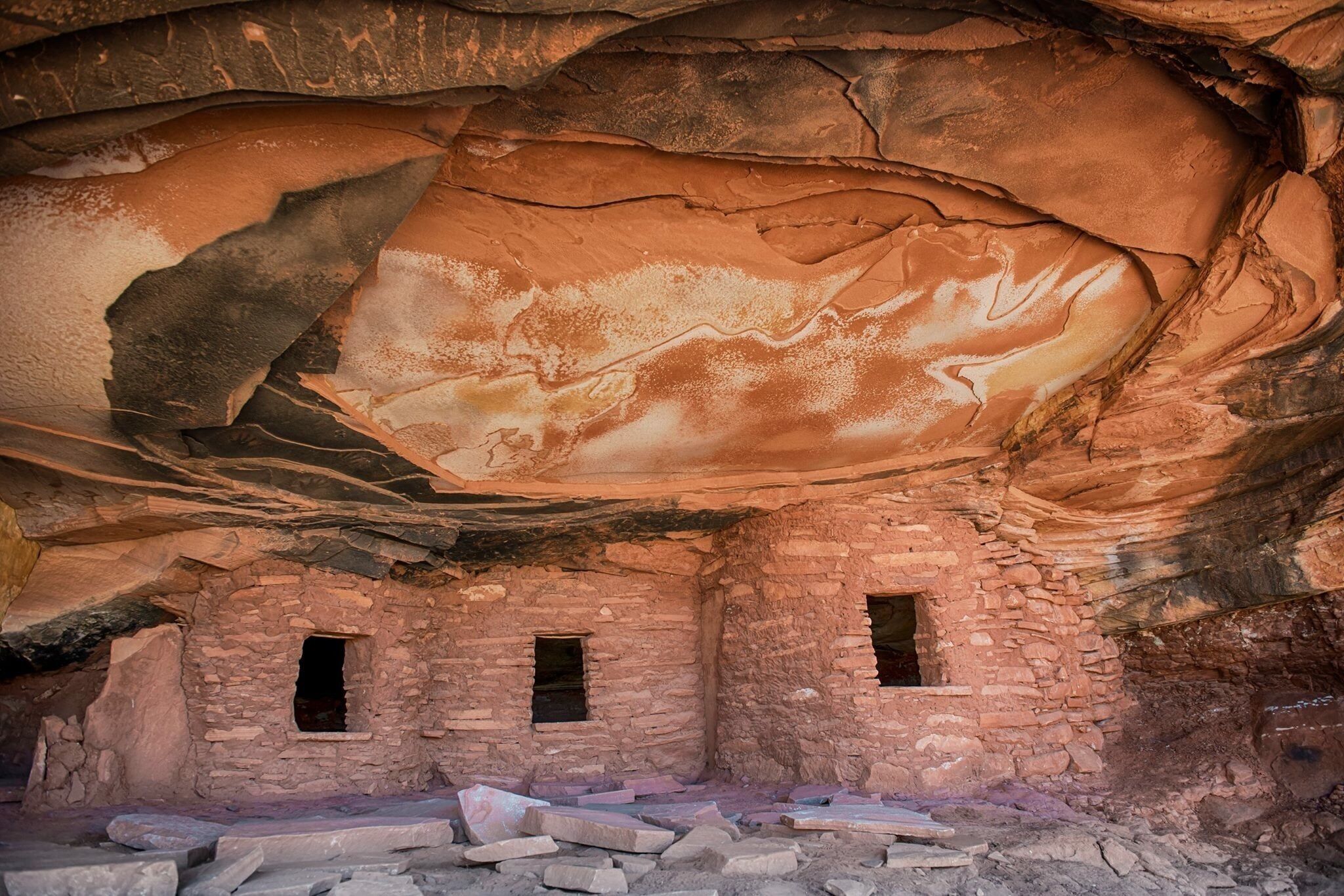 An ancient rock shelter with three small openings and scattered stone debris.