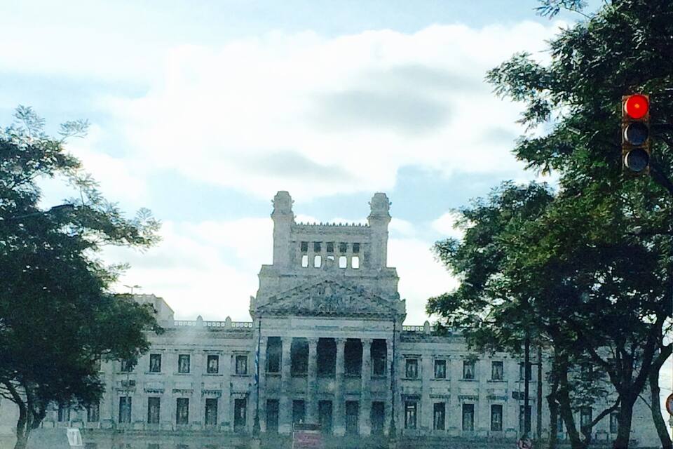A large, historic building with a central tower and columns, surrounded by trees and parked cars.