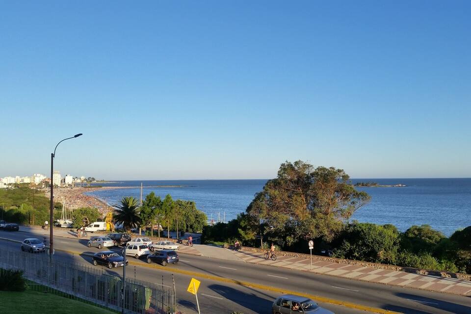 A coastal road with vehicles, a beach, and a clear blue sky.