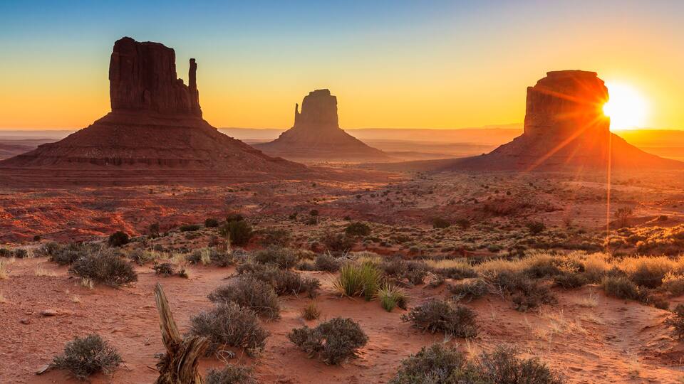 A desert landscape with three prominent rock formations during sunset.