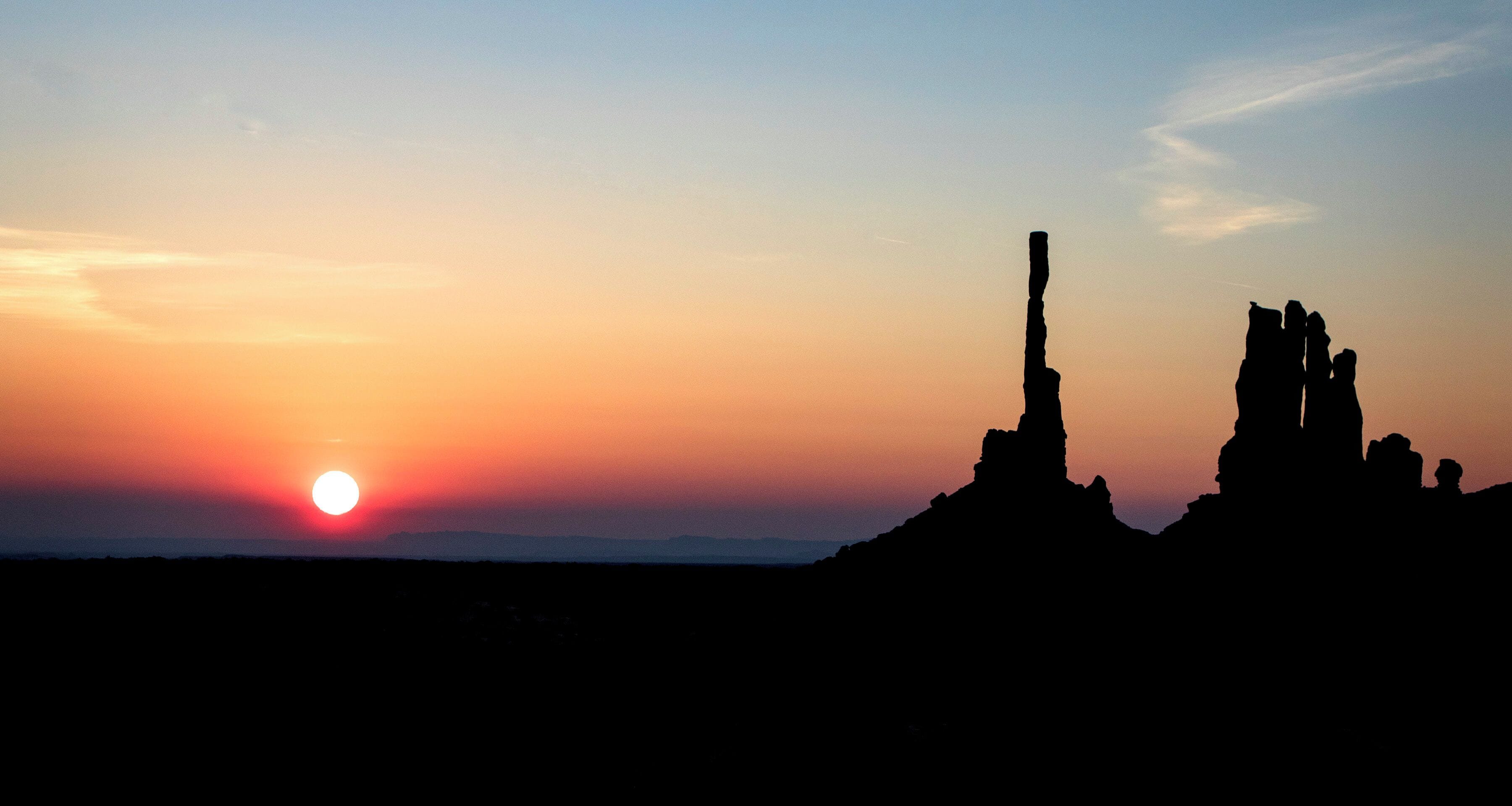 A sunset over a rocky landscape with prominent rock formations silhouetted against the sky.