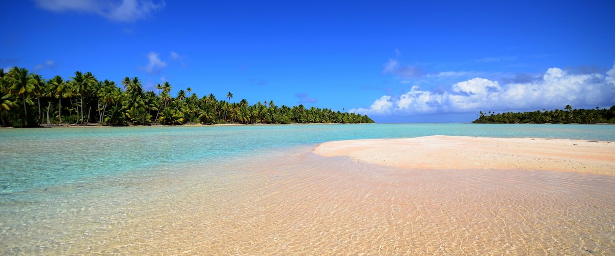 A tropical beach with clear turquoise waters, a sandy shore, and palm trees lining the coastline.