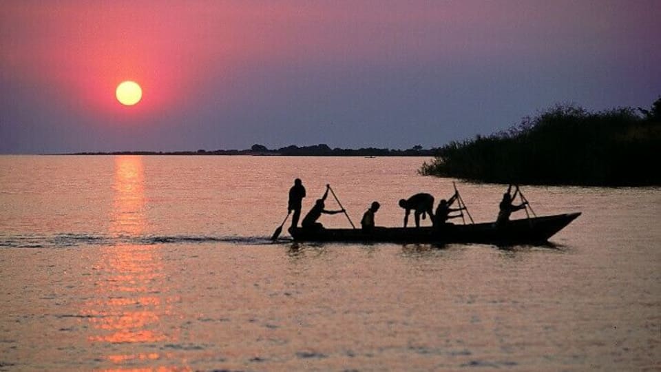 A sunset over a calm body of water with a small boat carrying people and a dog.