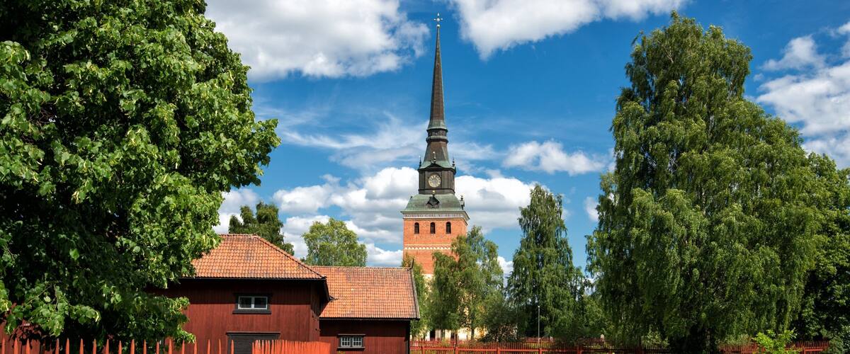 A church with a tall steeple, surrounded by lush greenery and a red fence.