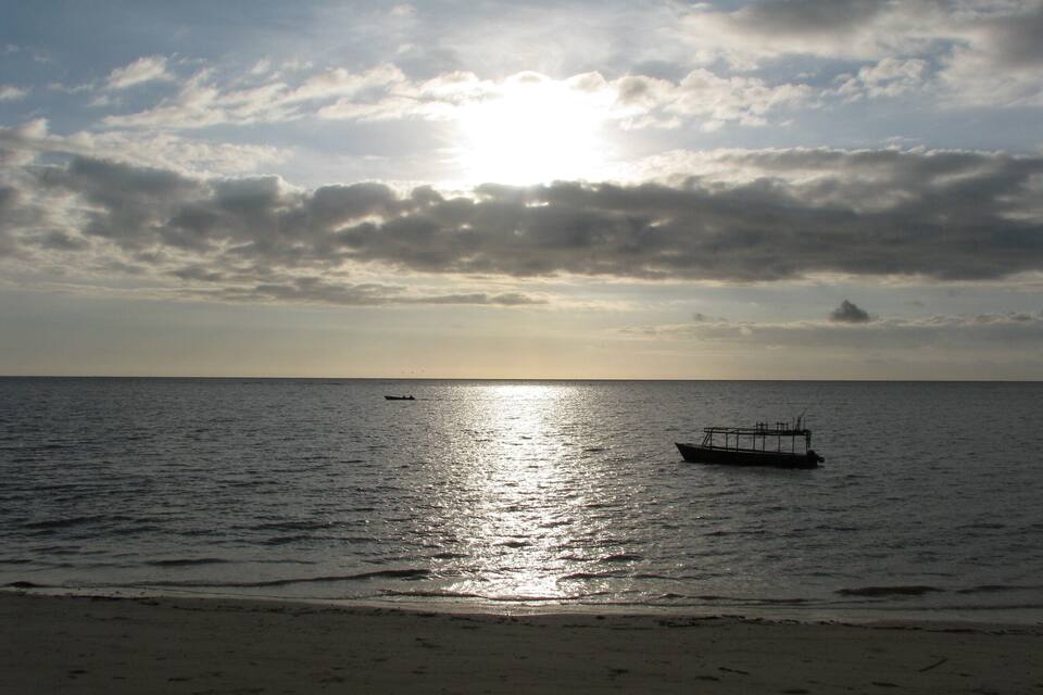 A beach with a boat on the water and the sun setting in the background.