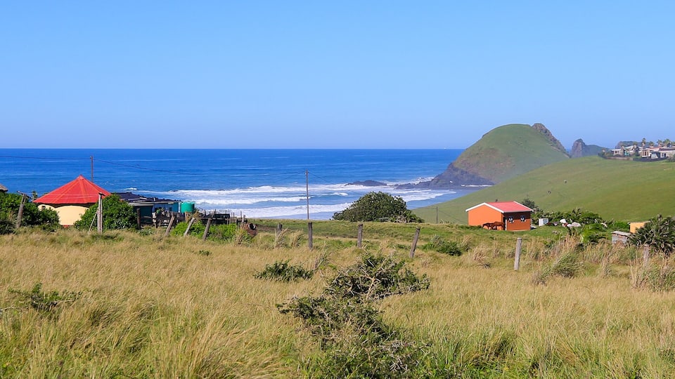 A coastal village with thatched-roof houses, a grassy hill, and the ocean.