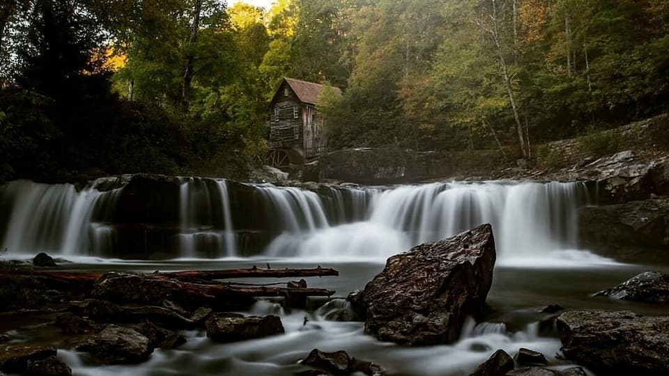 A waterfall with a rustic cabin in a forested area.