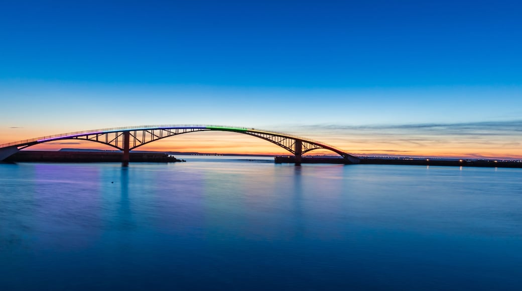 A bridge spanning a calm body of water at sunset.