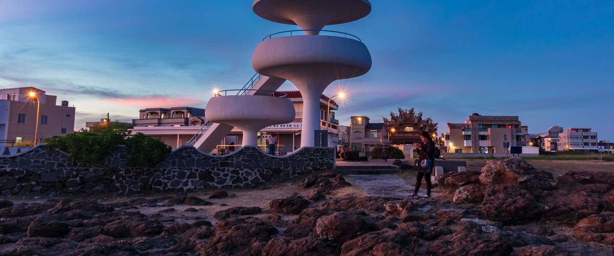 A modern architectural structure with a circular design, surrounded by rocky terrain and residential buildings in the background.