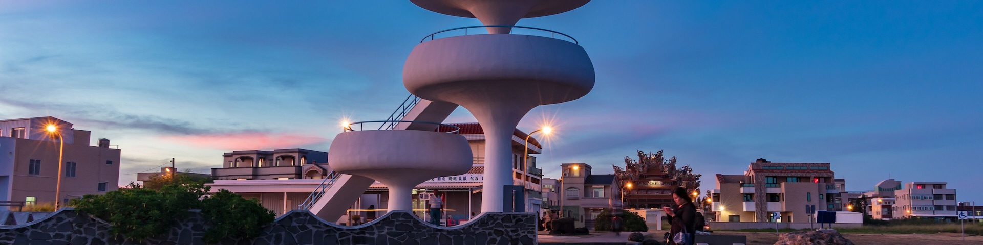 A modern architectural structure with a circular design, surrounded by rocky terrain and residential buildings in the background.