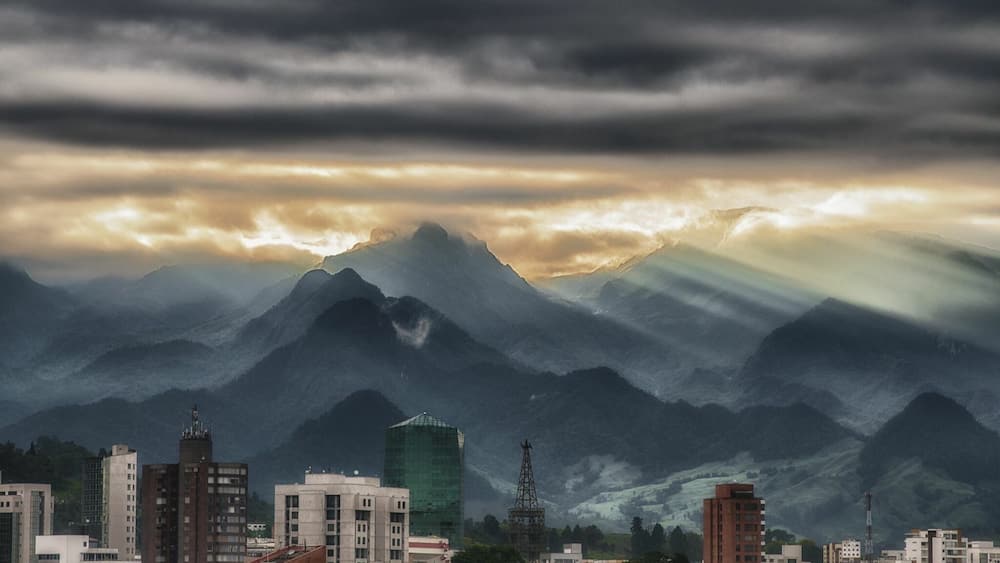 A cityscape with mountains in the background under a cloudy sky.
