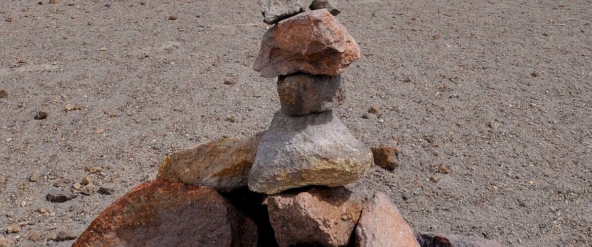 A stack of rocks on a sandy beach with a mountainous background.