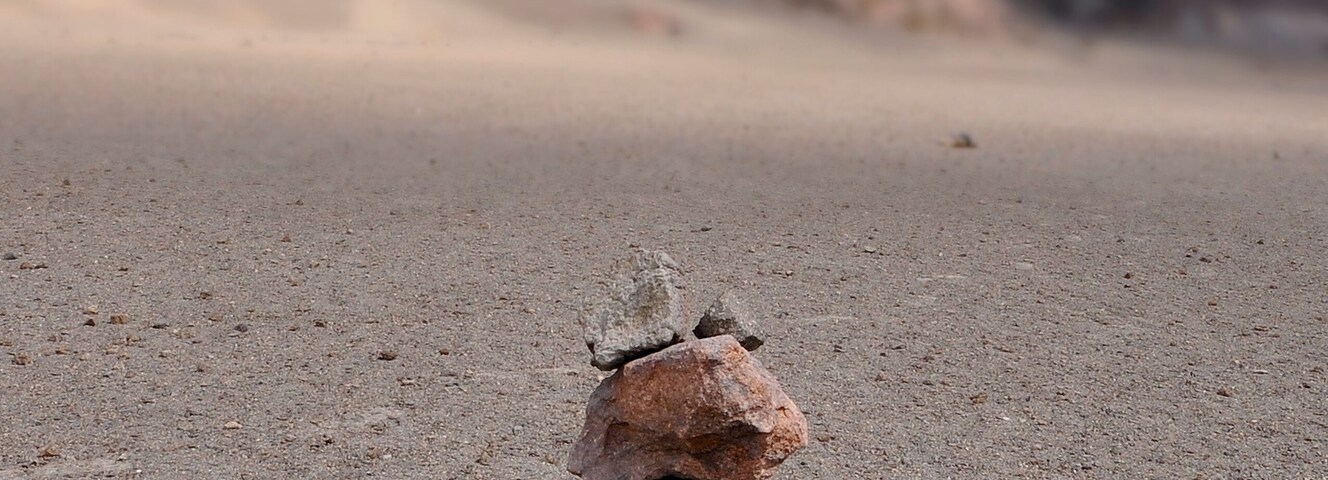A stack of rocks on a sandy beach with a mountainous background.