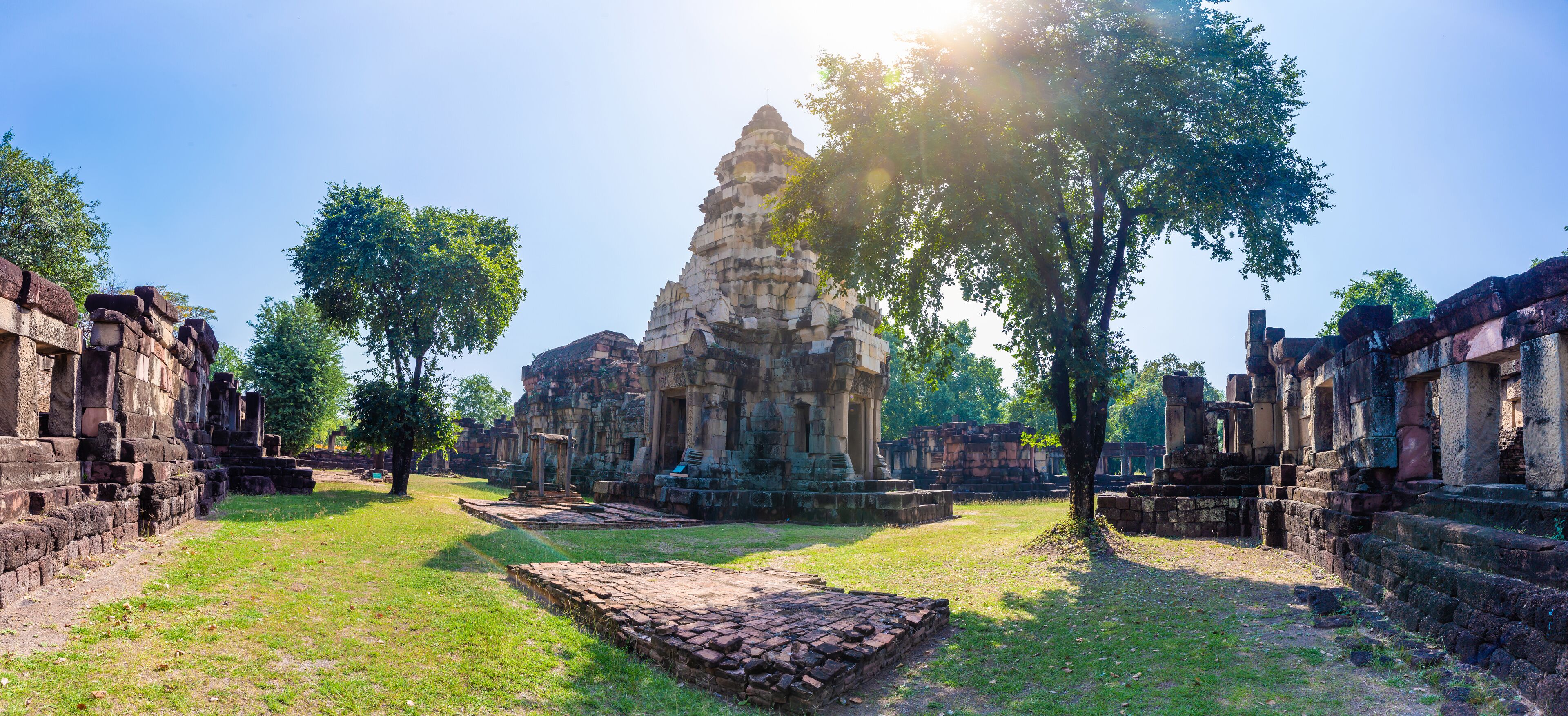Ancient stone ruins with a central temple structure, surrounded by trees and grassy areas.