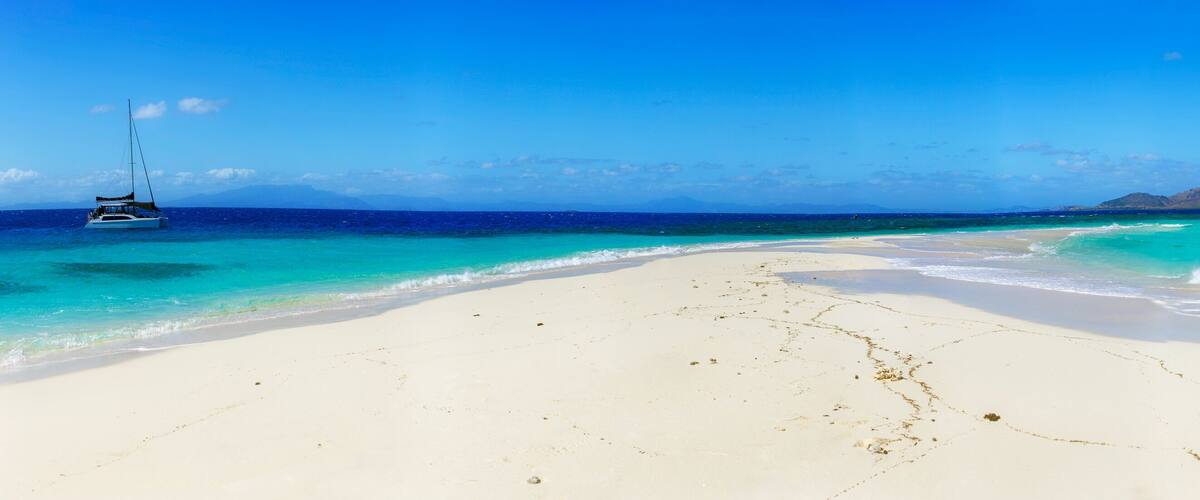 A white sandy beach with turquoise waters, a sailboat, and distant islands.