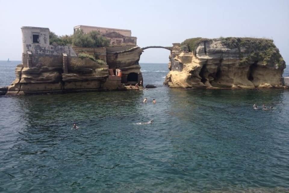 Formació rocosa a la costa amb edificis a dalt i un mar blau i translúcid.